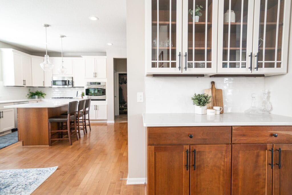 Natural wood grain oak wood cabinets with white uppers with kitchen in the background