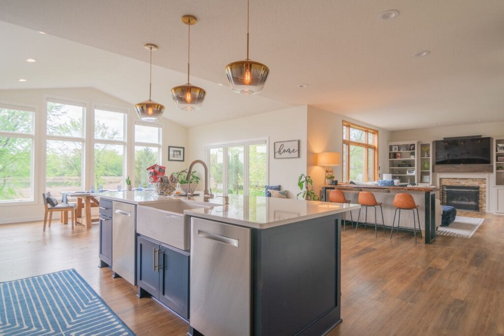 Light fixtures and w a dishwasher and white quartz counter inside a kitchen and living room in the background.