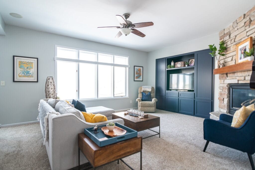 Living room with ceiling fan and blue walls with large window full of day light.