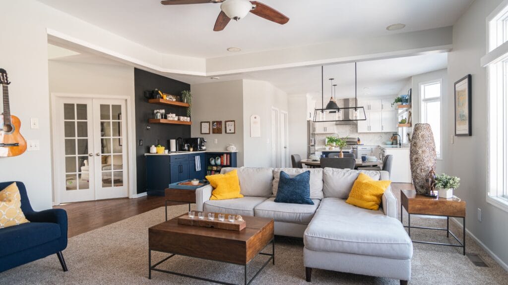 Living room with a bar corner in the background with kitchen and crown molding and recessed lighting.