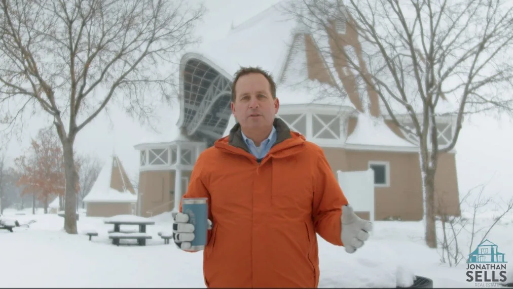 Jonathan Sells standing in front of the harriet bandshell in the winter with a coffee mug in his right hand wearing and orange coat