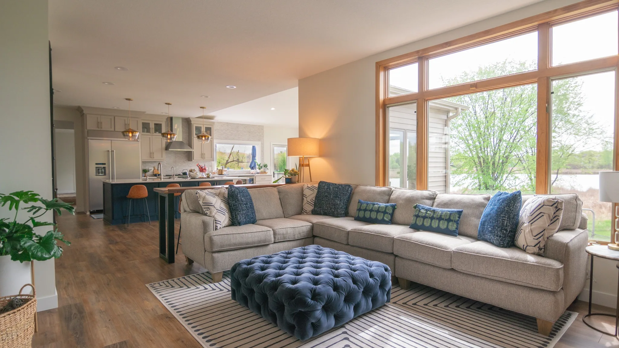 Living room with a soft looking ottoman and white couch and large windows in the background.