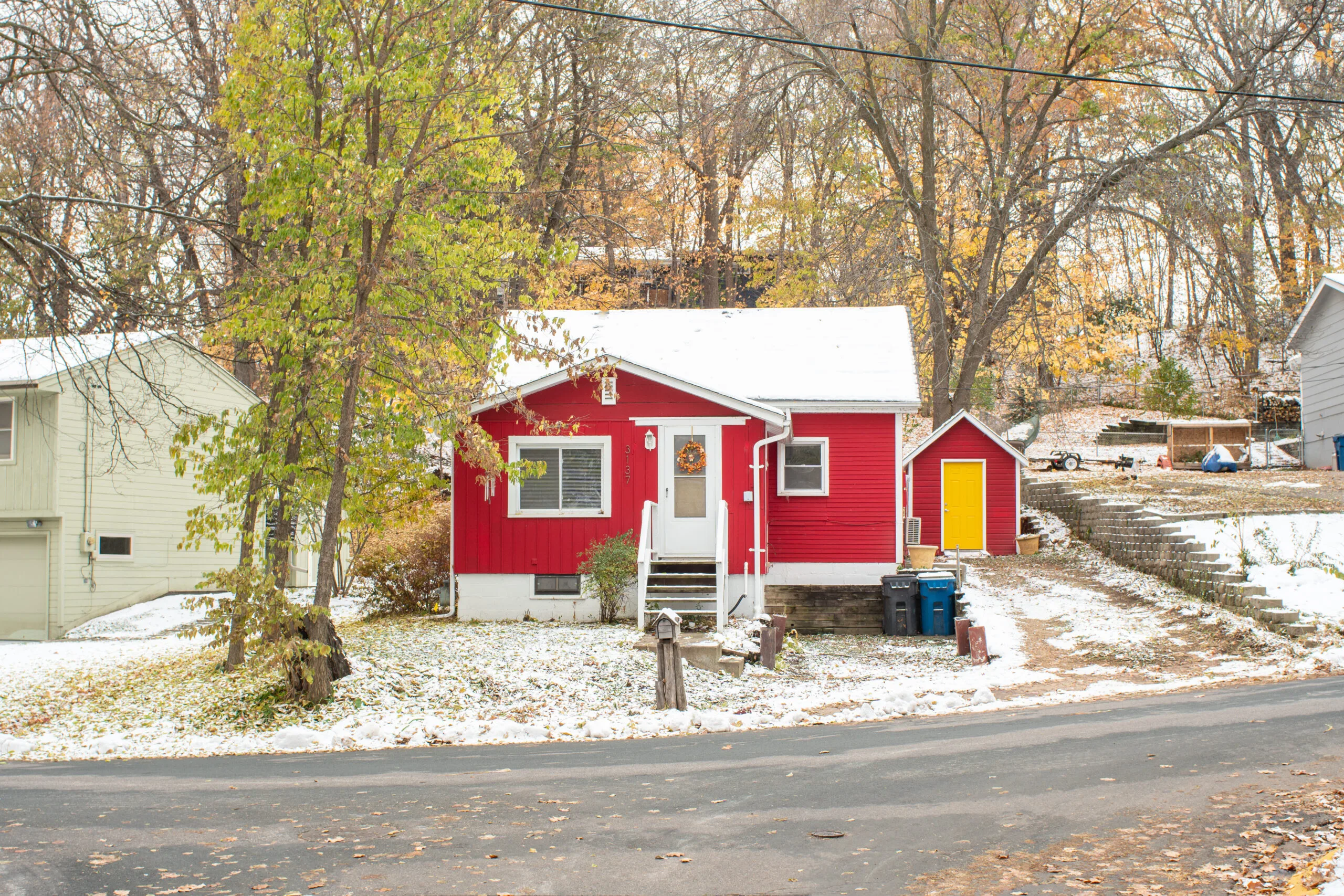 Red House with yellow door and snow on the ground with a garage in the background