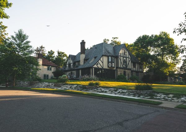 Wide angle of a tudor style house with a plane in the background and sunset light going over the green grass.